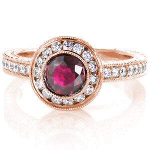 Rose gold and ruby engagement ring in Austin. This perfect combination of the warm rose gold hues, and the red sapphire center stone are exquisitely crafted with a diamond band and diamond halo. This antique engagement ring style also feature hand engraving, hand formed filigree curls, and small bezel set surprise diamonds.